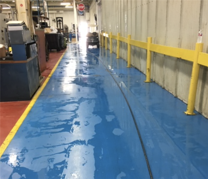 Commercial warehouse facility with blue flooring pooled with water after a loss.