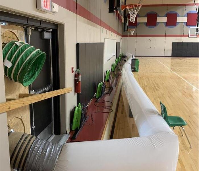 Green drying equipment and air tube set up along the floor of a gym of a local school.